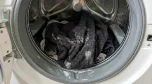 Interno di una lavatrice con asciugamani scuri e residui di detersivo sul bordo dell’oblò